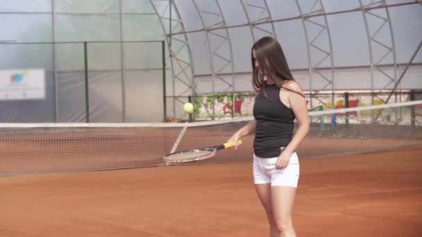 Brunette woman hitting the tennis ball off the racket on the court. Mid shot - 映像、動画