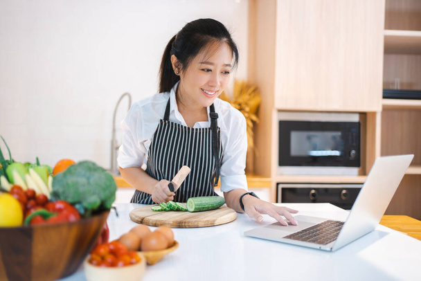 Woman in kitchen following recipe on digital laptop - Photo, image