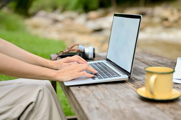 Cropped image, Female relaxing in the natural green parkland, sitting near the river and using laptop computer. - Foto, Imagen