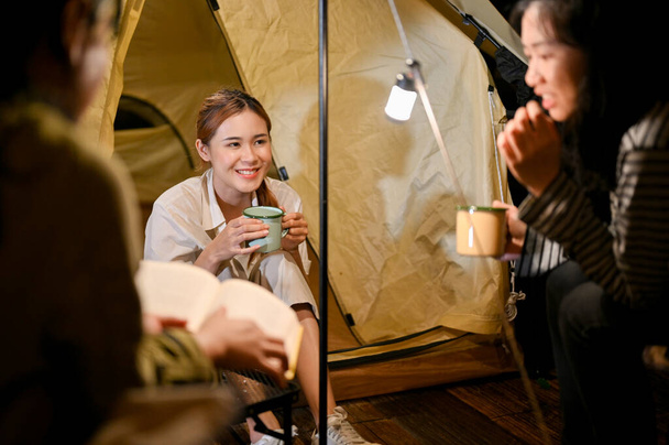 Vonzó fiatal ázsiai nő élvezi a beszélgetést, hogy egy kellemes beszélgetés a barátaival éjszaka kempingezés közben együtt a kemping. - Fotó, kép