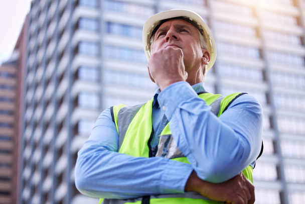 Whats the best way forward here. Low angle shot of a handsome mature male construction worker looking thoughtful while standing outside - Фото, изображение