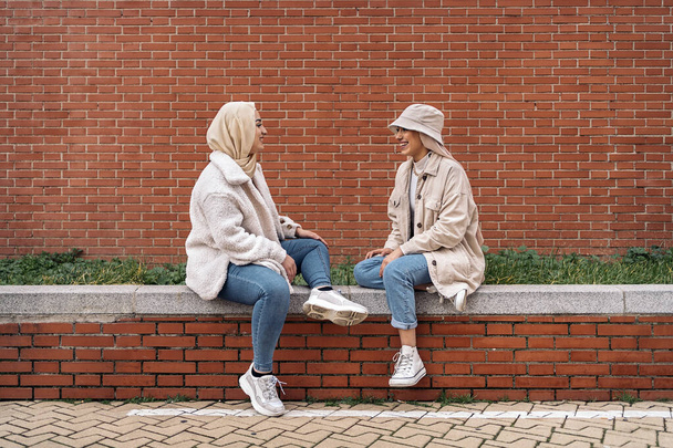 Cheerful young women wearing hijab talking and sitting in a bench. - Foto, Imagem