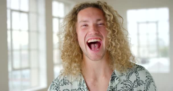 Portrait of a joyful young man laughing and being amused by a joke. Face of a handsome and confident male standing in a bright room. Closeup of a casual and positive guy looking happy and content. - Metraje, vídeo