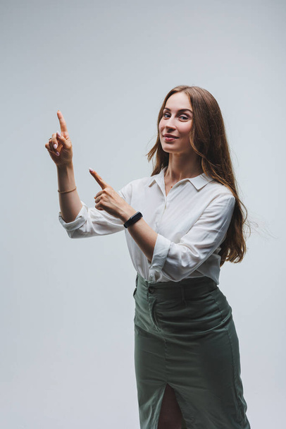 Smiling woman in white shirt recommends opt for advertising index finger to side on workspace, commercial promo area, copy space mockup isolated on white background - Fotó, kép