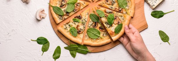 Female hand taking slice of tasty pizza from wooden board, top view - Foto, Imagem