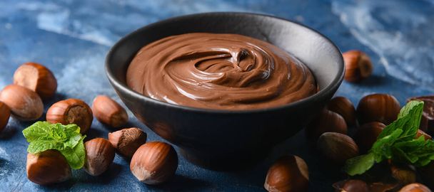 Bowl with tasty chocolate paste and hazelnuts on blue background - Photo, Image