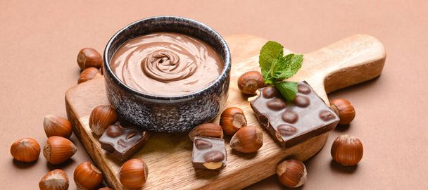 Tigela com pasta de chocolate saborosa e avelãs no fundo de cor - Foto, Imagem