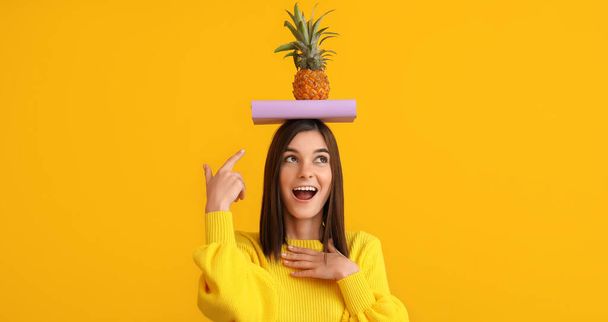 Schöne glückliche junge Frau mit Buch und Ananas auf gelbem Hintergrund - Foto, Bild
