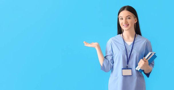 Female medical student with books showing something on blue background with space for text - Photo, Image