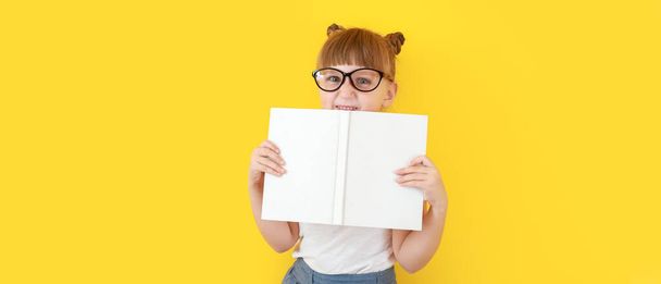 Милая маленькая девочка с книгой на желтом фоне - Фото, изображение