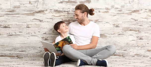 Vater und kleiner Sohn lesen Buch an Holzwand - Foto, Bild
