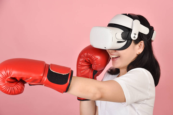 Asian woman hitting a punch by vr glasses, Working out with boxing video games application from virtual reality headset, Young woman enjoy new fitness experience by vr technology, Studio shot. - Foto, imagen