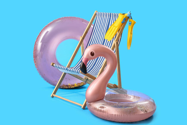 Wooden deck chair with inflatable rings and paddles on blue background - 写真・画像