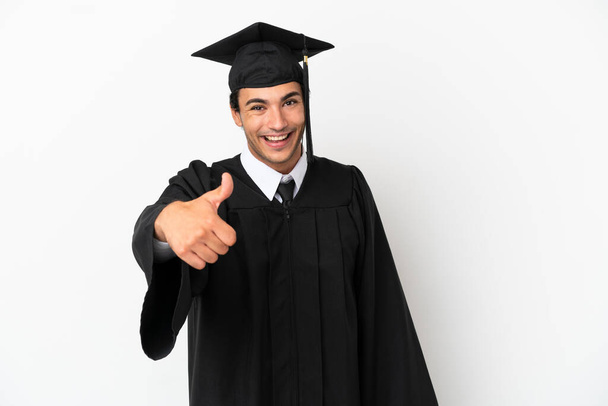 Молодой выпускник университета на изолированном белом фоне с большими пальцами вверх, потому что что-то хорошее произошло - Фото, изображение