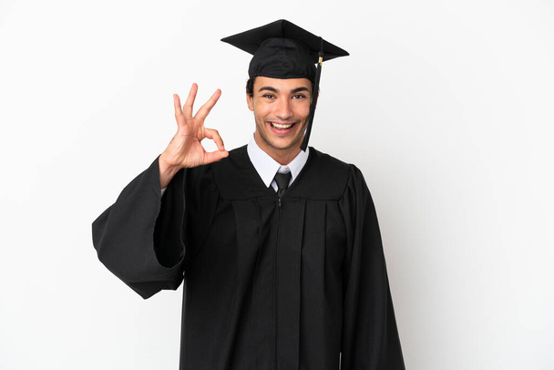 Mladá univerzita absolvent přes izolované bílé pozadí ukazující ok znamení s prsty - Fotografie, Obrázek