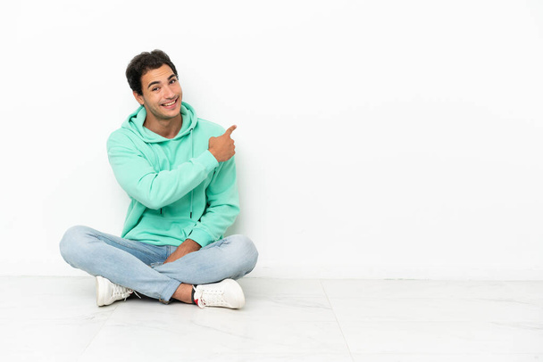 Caucasian handsome man sitting on the floor pointing back - Foto, immagini