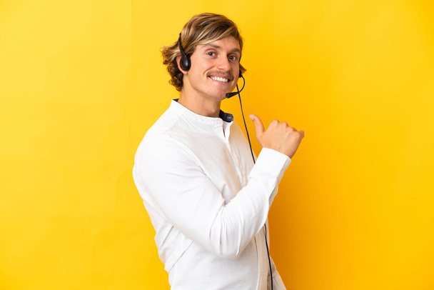Telemarketer man working with a headset isolated on yellow background proud and self-satisfied - Фото, изображение