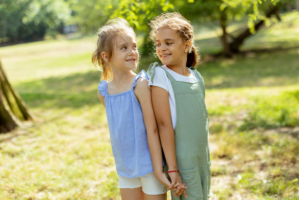 Two cute little girls standing back to back in the park - Fotoğraf, Görsel