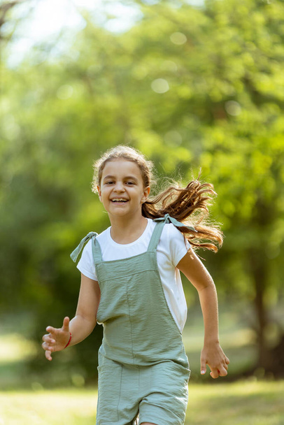 Милая маленькая девочка, счастливо бегающая в парке - Фото, изображение