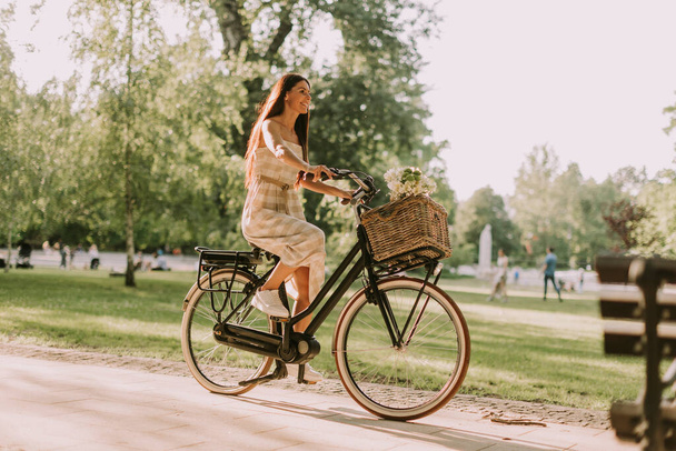 Sepetinde çiçeklerle elektrikli bisiklete binen güzel genç bir kadın. - Fotoğraf, Görsel
