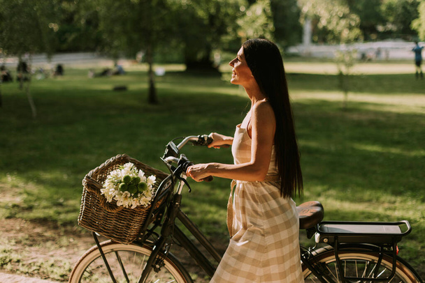 Mujer joven y bonita con flores en la cesta de la bicicleta eléctrica - Foto, Imagen