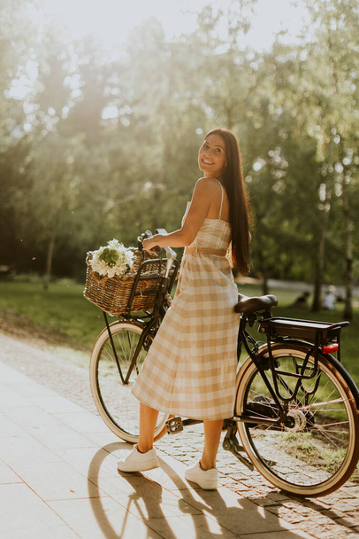Pretty young woman with flowers in the basket of electric bike - Photo, Image