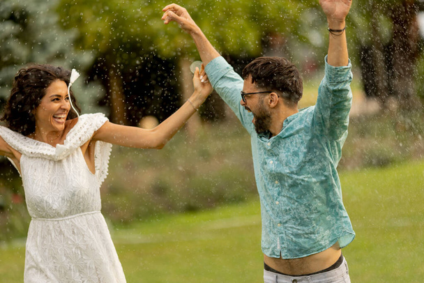 Joyful young couple caught by the sudden summer rain in the park - 写真・画像