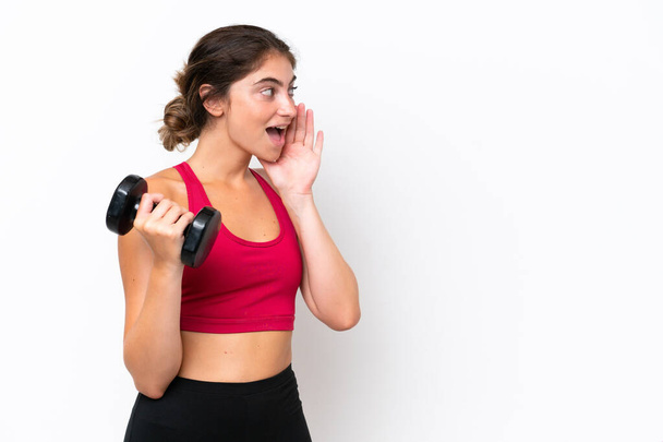 Young sport caucasian woman making weightlifting isolated on white background shouting with mouth wide open to the side - 写真・画像