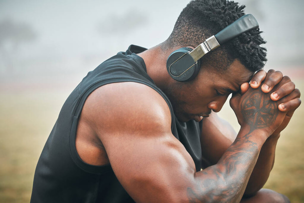 Take a moment to gain your focus again. a muscular young man wearing headphones while exercising outdoors - Foto, afbeelding