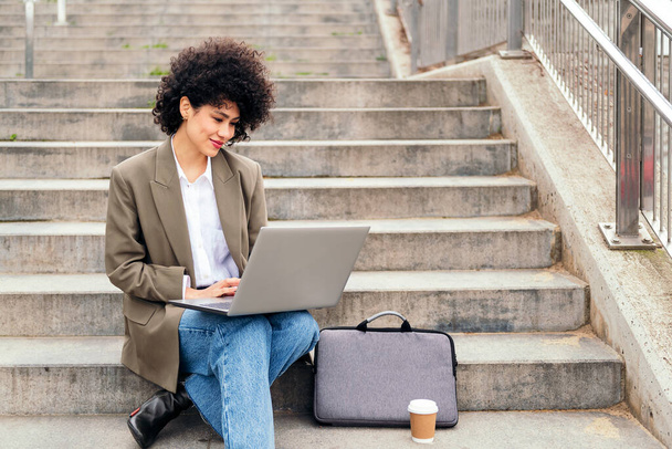 young latin woman working with her laptop computer sitting on a city staircase, concept of business and urban lifestyle - Fotografie, Obrázek