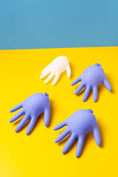 Three purple and one white inflated latex gloves on a vibrant yellow surface on a bright blue background in a studio. Closeup vertical photo. - Photo, image