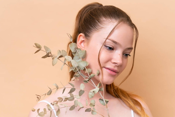 Young caucasian girl isolated on beige background holding a eucalyptus branch. Close up portrait - Photo, Image