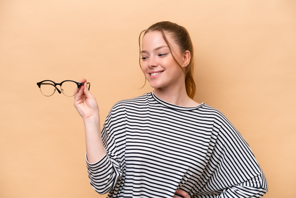 Young caucasian girl with glasses isolated on beige background with happy expression - Fotografie, Obrázek