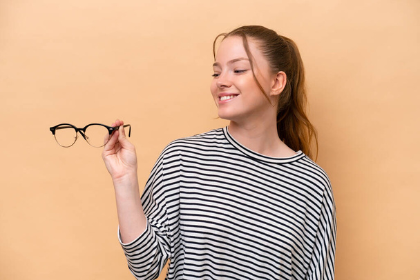 Young caucasian girl with glasses isolated on beige background with happy expression - Photo, Image