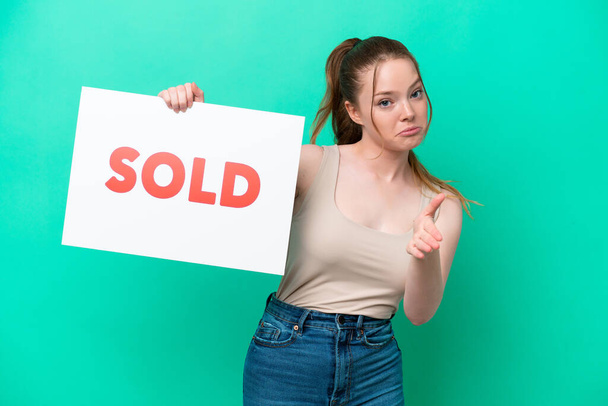 Young caucasian woman isolated on green background holding a placard with text SOLD making a deal - Foto, imagen