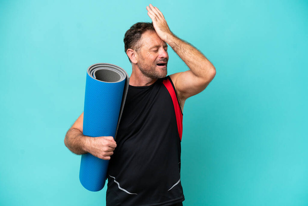 Middle age sport man going to yoga classes while holding a mat isolated on blue background has realized something and intending the solution - 写真・画像
