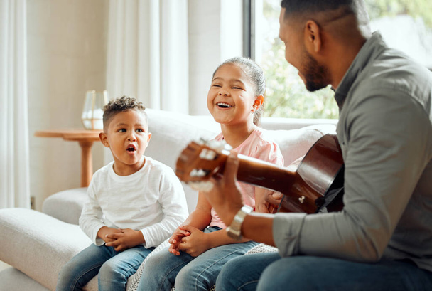 Were dads biggest fans. a young father teaching his kids how to play the guitar while sitting on the sofa at home - Foto, immagini