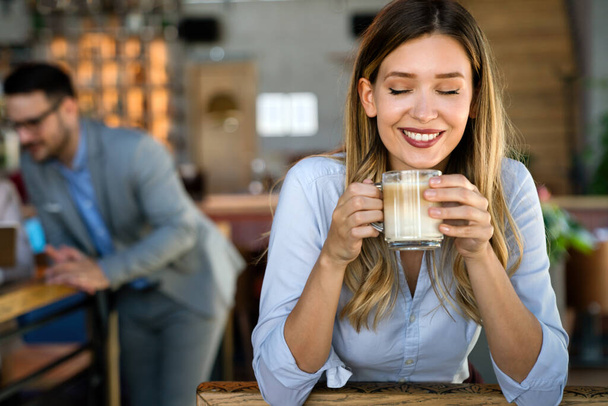 Portrait of happy young successful business woman drinking coffee in a break. In the background, her colleagues - Foto, Imagem