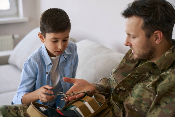 Katonai kiképző fiú, aki orvosi segítséget nyújt, és ollót ad neki kezelésre. - Fotó, kép