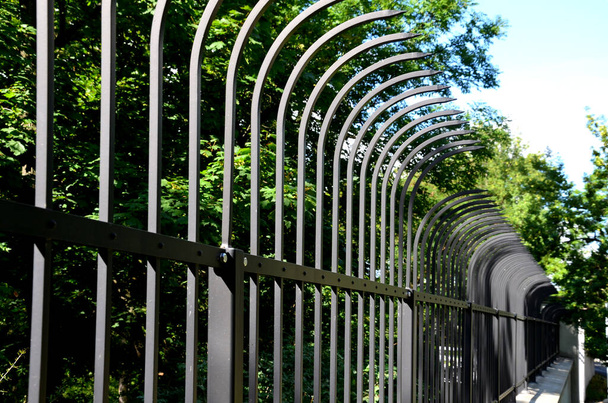 fencing of building from forged bars with curved spikes. military guarded bases and an embassy with increased protection against overcoming inward encirclement. black bars on fence with dangerous - Foto, Bild