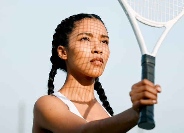 Eyes on the prize. a sporty young woman shielding her face from the sun with a tennis racket on a court - Photo, Image