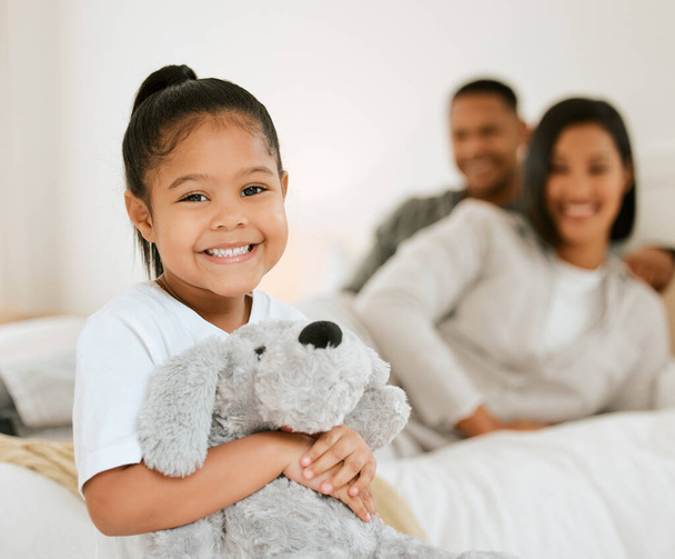 Their favourite toy makes bedtime easier. Portrait of a young family settling in for bedtime while their daughter poses with a teddy in bed at home - Foto, imagen