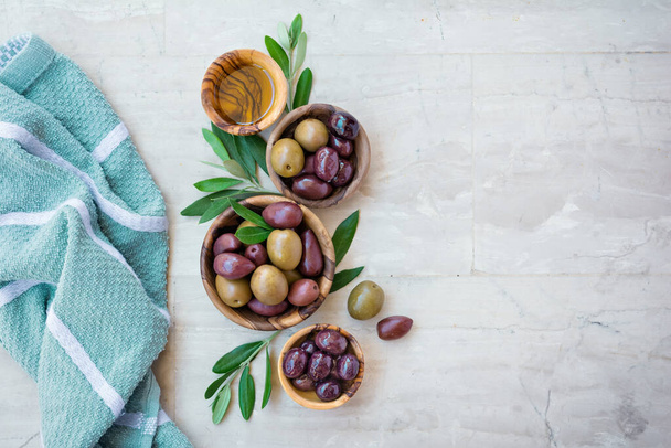Tasty olives and oil in wooden bowls with green branches on light background with copy space - Foto, Bild