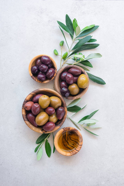 Tasty olives and oil in wooden bowls with green branches on light background - Photo, Image