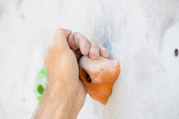 Close-up of a male hand smeared with magnesium powder grabbing a hold of a climbing wall. - Fotó, kép