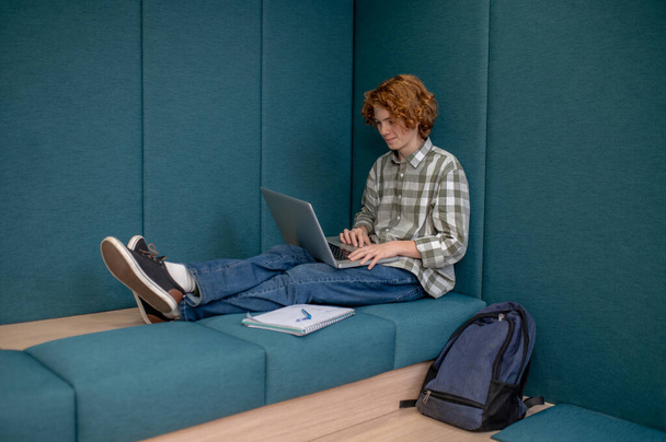 Online. Ginger boy sitting with a laptop and watching something online - Foto, imagen