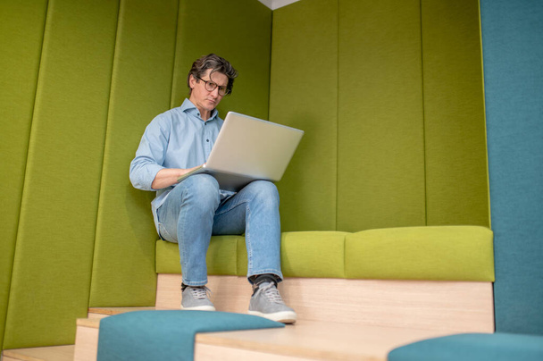 In a lounge zone. A man in eyewear sitting with a laptop in a lounge zone - Foto, imagen