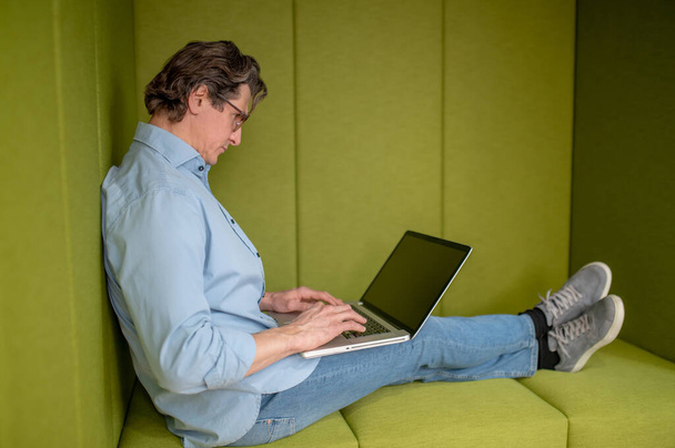In a lounge zone. A man in eyewear sitting with a laptop in a lounge zone - Photo, image