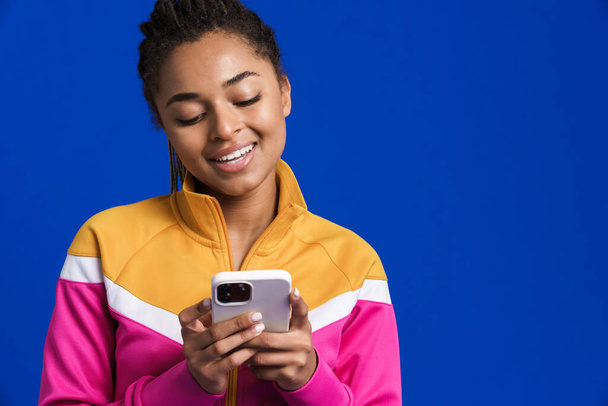 Black young woman smiling and using mobile phone isolated over blue background - Photo, image
