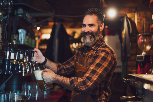 Portret wesołego barmana w pubie. Wlewa piwo do szklanki.. - Zdjęcie, obraz
